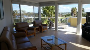 A spacious balcony with a glass table, leather sofas, and a TV stand. - Ultimate Holiday Apartments (Lakes Entrance)