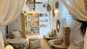 Una habitación acogedora y bien iluminada con una cama, zona de estar y estanterías llenas de libros y objetos decorativos.