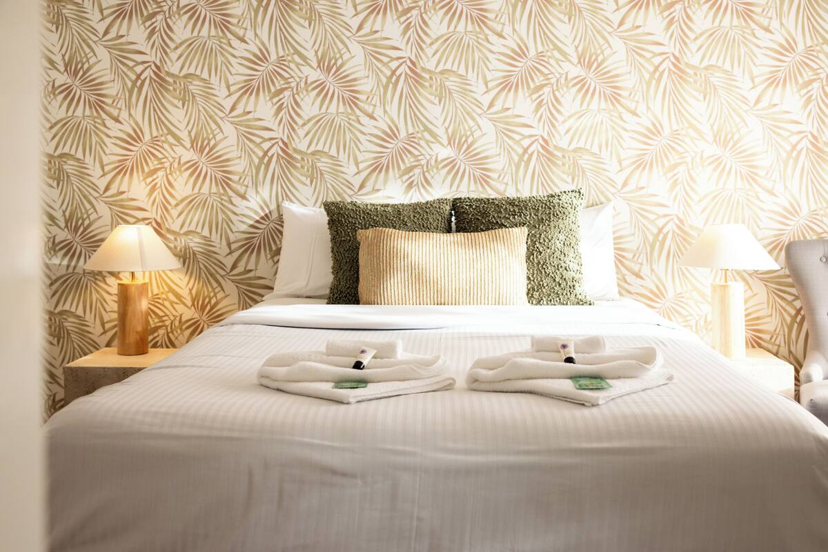 Una cama bien hecha con sábanas blancas, dos almohadas y un juego de toallas sobre la cama.