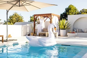 Una piscina con un flotador de cisne, un porche de madera y plantas en macetas.