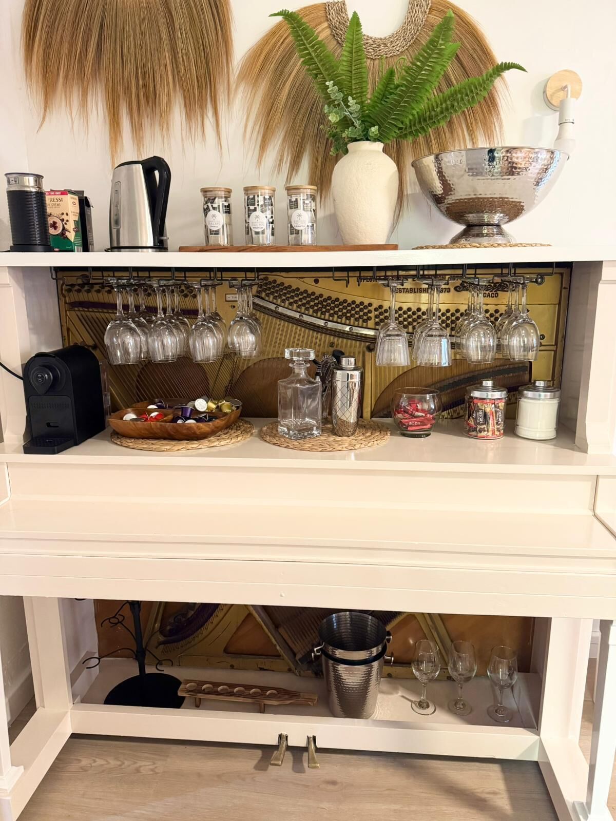 A kitchen counter with a coffee machine, jars, a bowl of fruit, and hanging wine glasses.