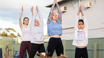 A group of people performing yoga on outdoor mats with a goat and a dog nearby.