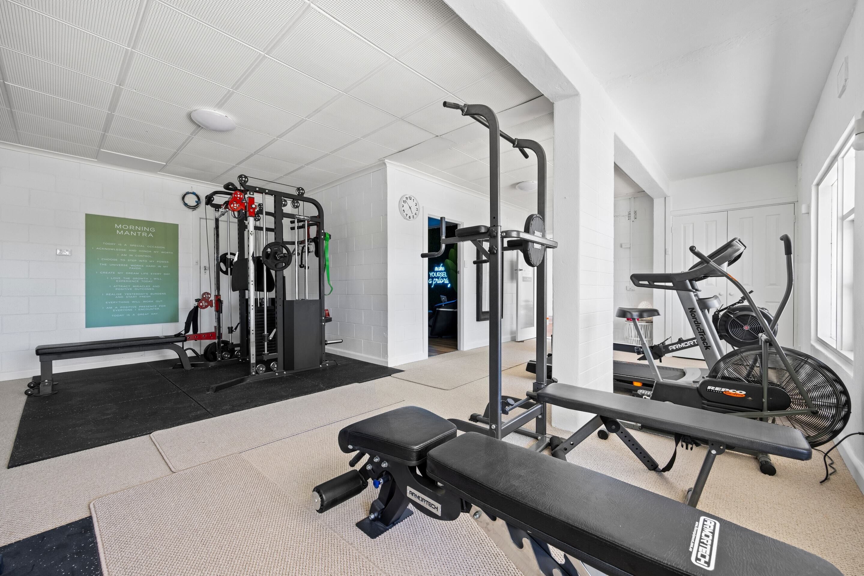 A gym with various exercise equipment, including a bench, a treadmill, and weight machines.