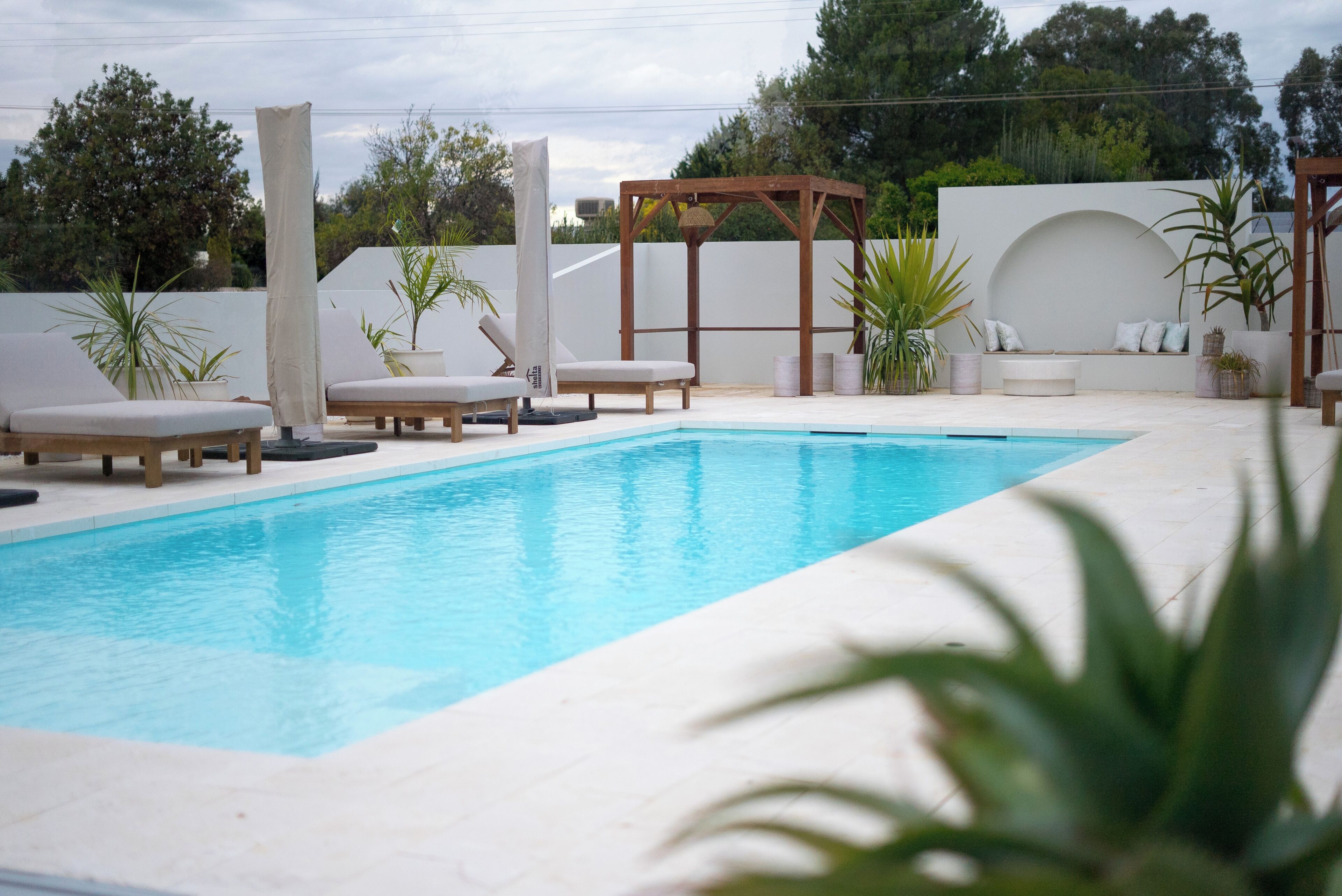 A rectangular pool with lounge chairs and a wooden pergola.