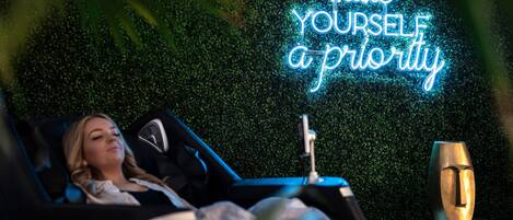 Uma pessoa relaxada em um carro de luxo, com um letreiro de neon ao fundo com a frase 'coloque-se em primeiro lugar'.