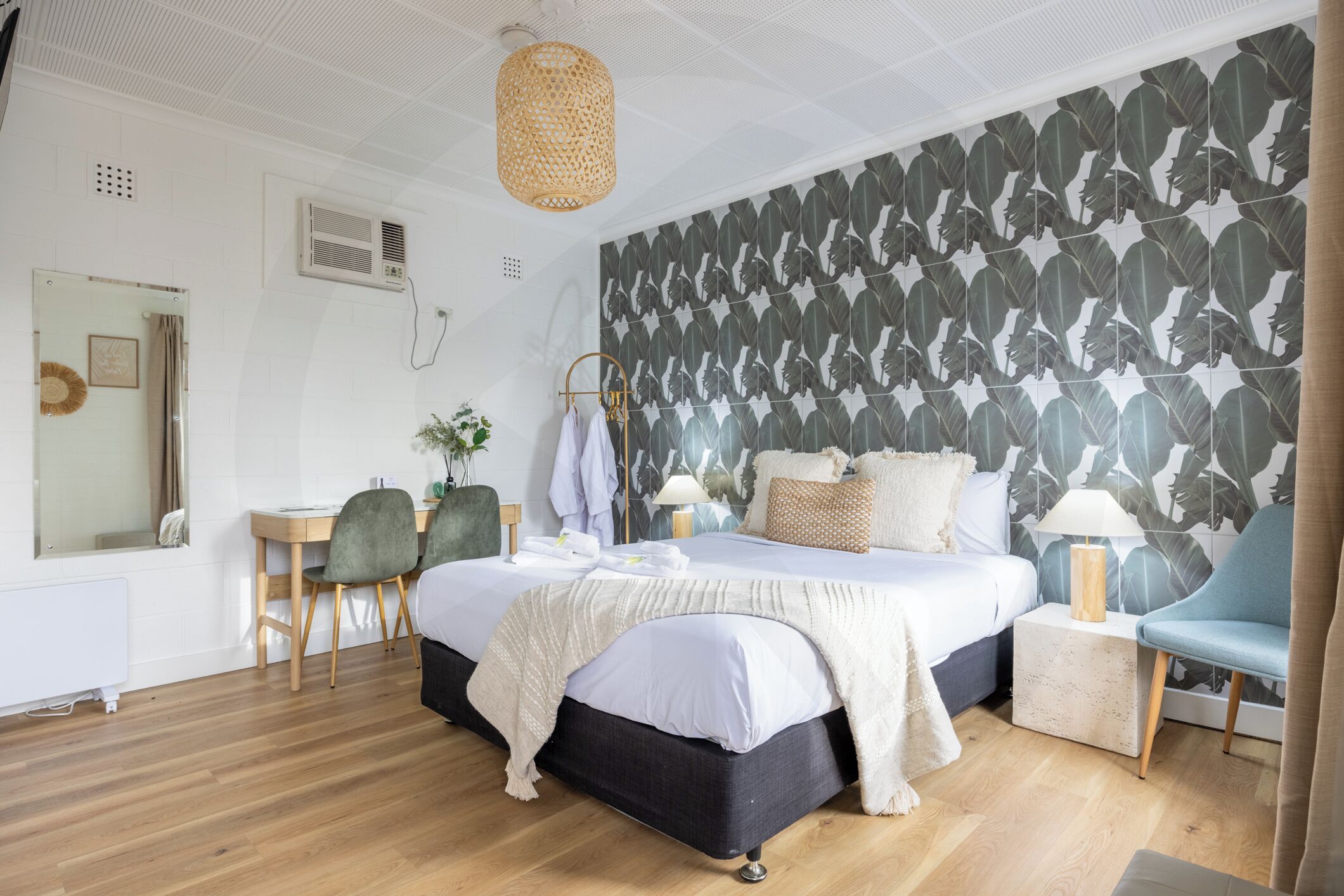 A bedroom with a large bed, a desk, a chair, and a wall with a leaf pattern.