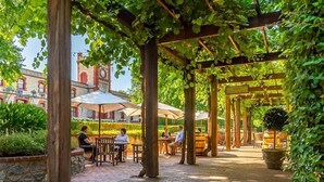 Café al aire libre con pérgolas de madera, mesas y sillas bajo una cubierta.