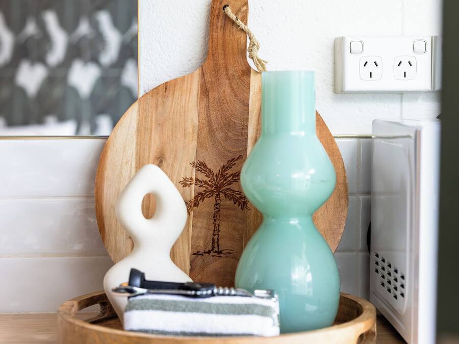 Una encimera de cocina con una tabla de cortar de madera, un jarrón azul turquesa y un utensilio de cocina blanco.