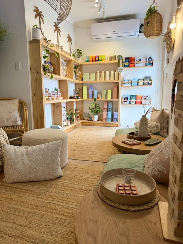 Una sala de estar acogedora con una estantería de madera llena de libros y adornos, un rincón de estar confortable con cojines, y una pequeña mesa de madera con una bandeja.