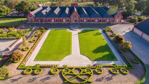 Un edificio grande e histórico, con jardines simétricos y un césped central.