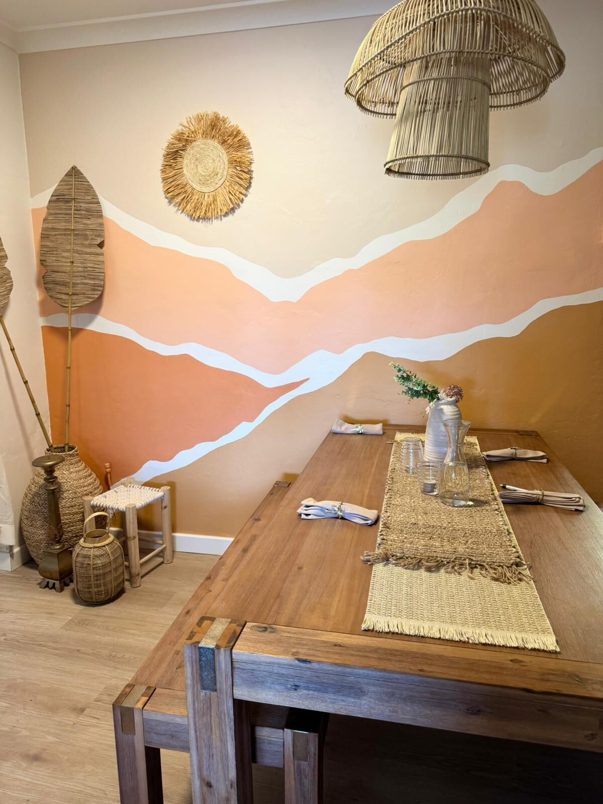 A dining area with a wooden table, woven placemats, and a wall mural depicting a desert landscape.