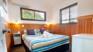 Une chambre à coucher avec un lit, deux tables de chevet, une commode, une fenêtre et une armoire blanche.