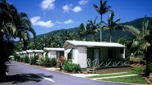 Une rangée de chalets blancs dotés de balcons, entourés d’une végétation luxuriante et de palmiers, le tout sur fond de montagnes.