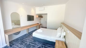 Une chambre d’hôtel avec un lit, une table de chevet, un miroir, une télévision et une salle de bain visible à travers une porte ouverte.
