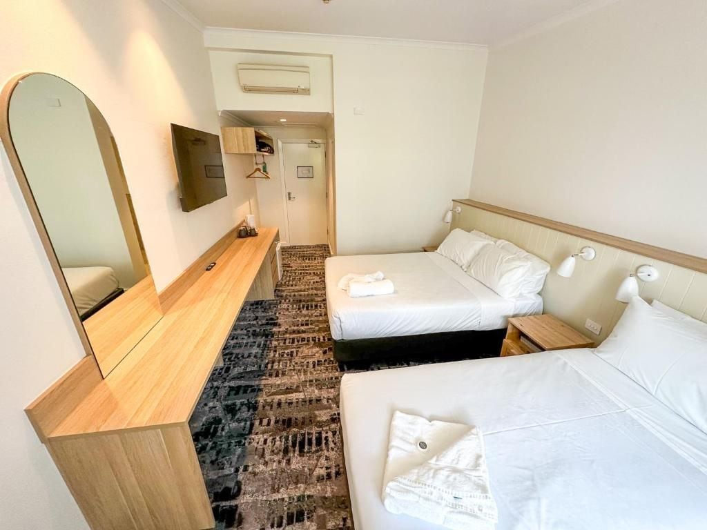 A hotel room with two beds, a wooden bench, a mirror, and a small table.
