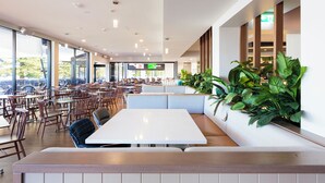 A spacious cafe with multiple seating areas, large windows, and indoor plants. - Pippi's At The Point (Speers Point)