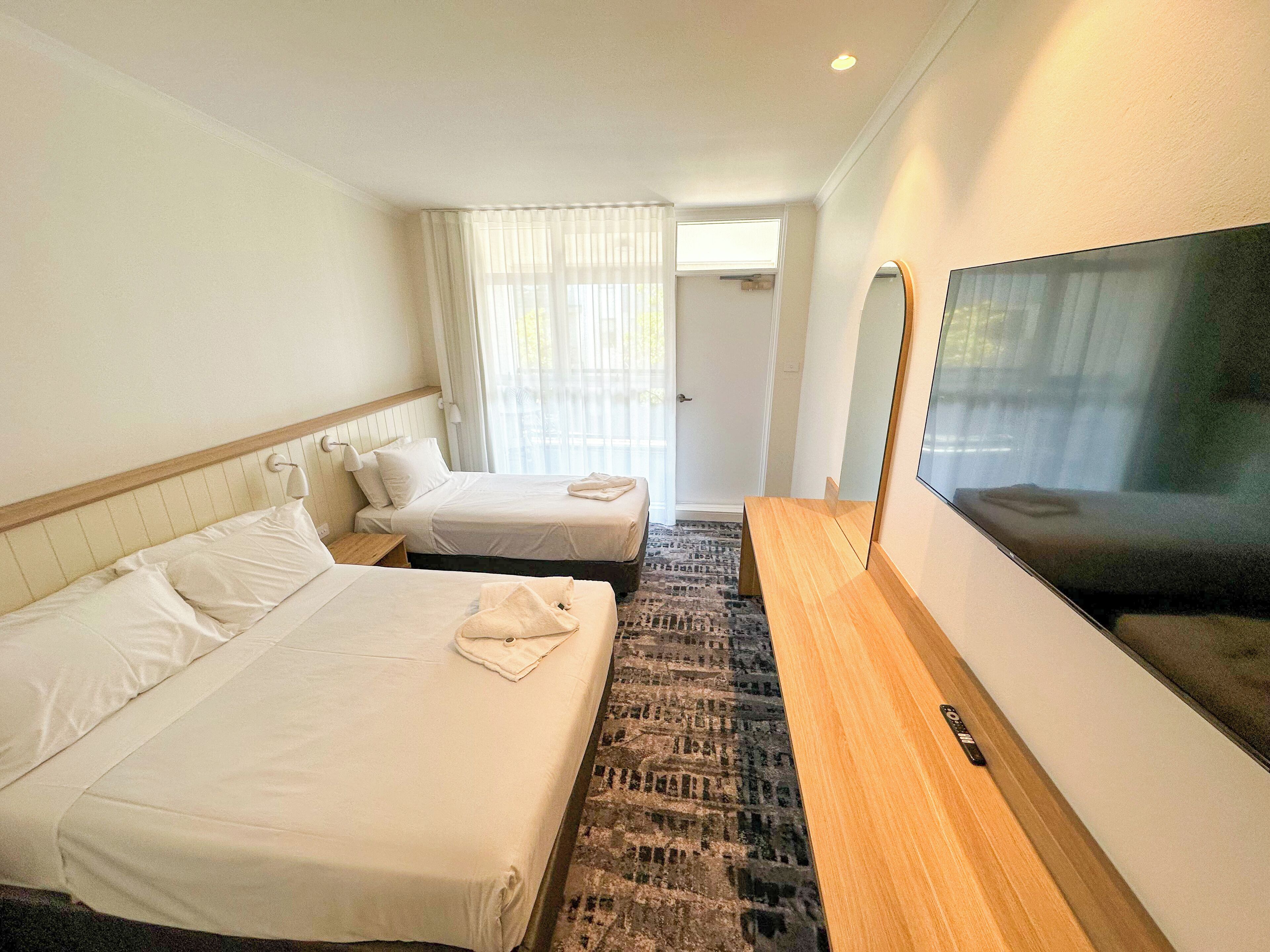 Habitación de hotel con dos camas, televisión y ventana con cortinas.