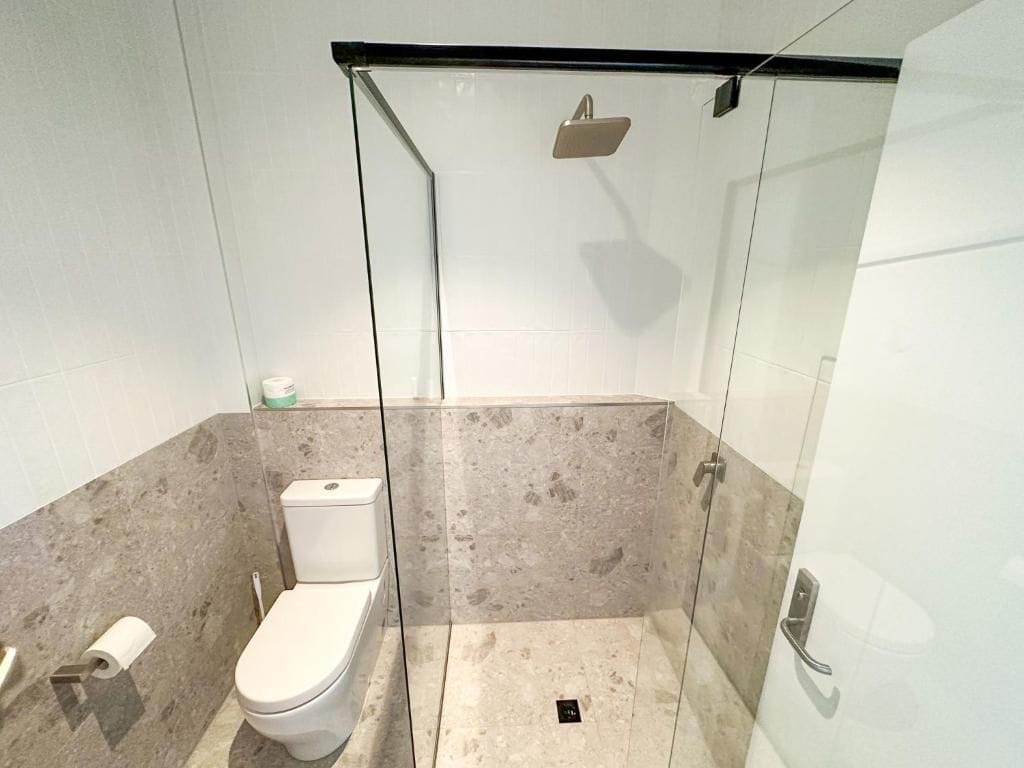 Een moderne badkamer met een glazen douchecabine, toilet en een marmeren vloer.
