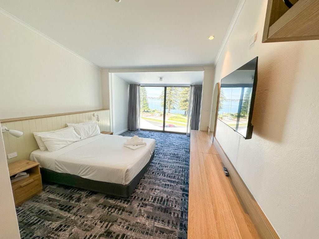 Habitación de hotel con una cama grande, un escritorio, una silla, un televisor de pantalla plana y vistas al exterior.