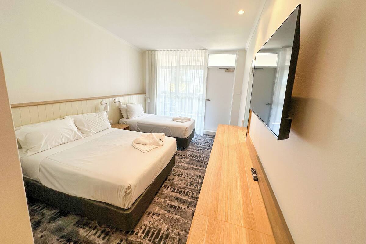 A hotel room with two beds, a large flat-screen TV, and a patterned rug.