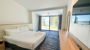 A hotel room with a large bed, a wooden nightstand, a desk, and a view of a body of water through a large window. - Pippi's At The Point (Speers Point)