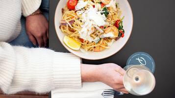 A person holding a wine glass and a menu, with a bowl of pasta in the background.