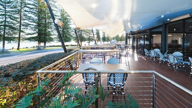 An outdoor seating area with tables and chairs, surrounded by greenery and trees. - Pippi's At The Point (Speers Point)