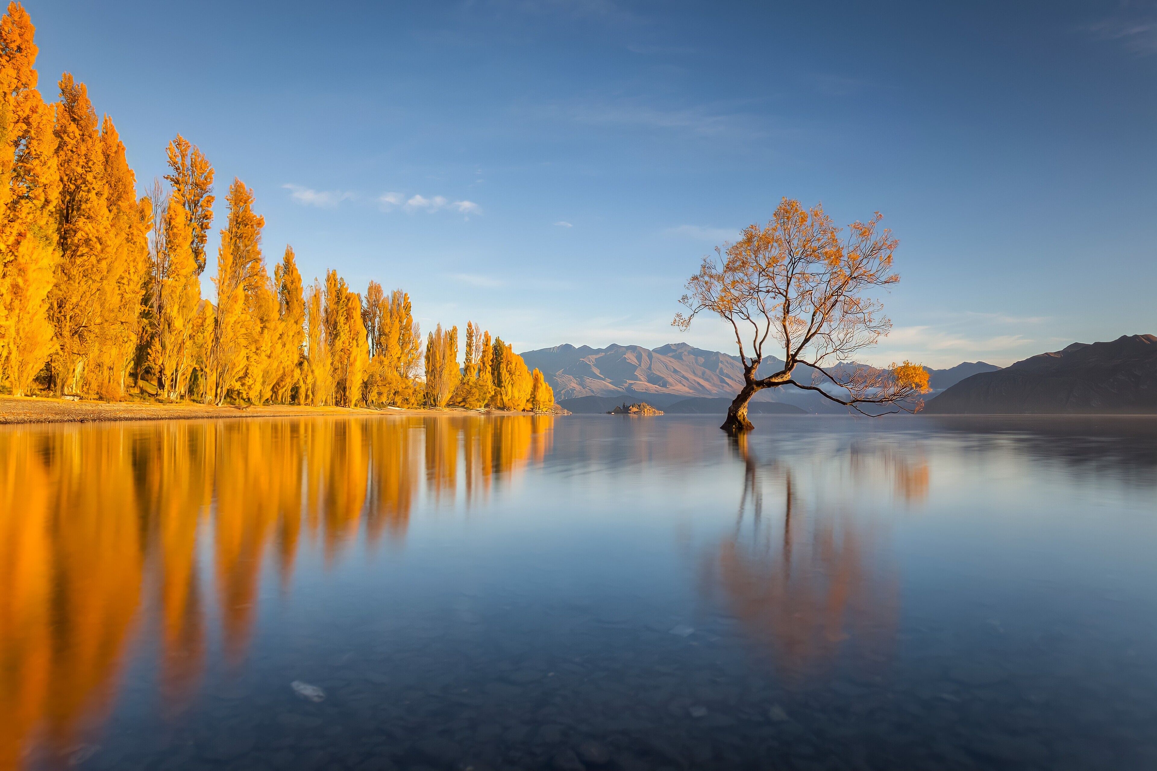 A tranquil lake with autumn trees reflecting on the water, surrounded by mountains.