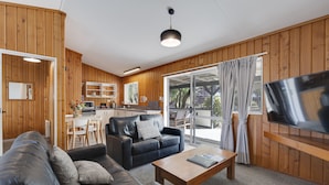 Una sala de estar moderna con un sofá, una mesa de centro y un televisor. Tiene paredes de madera y un ventanal con cortinas.