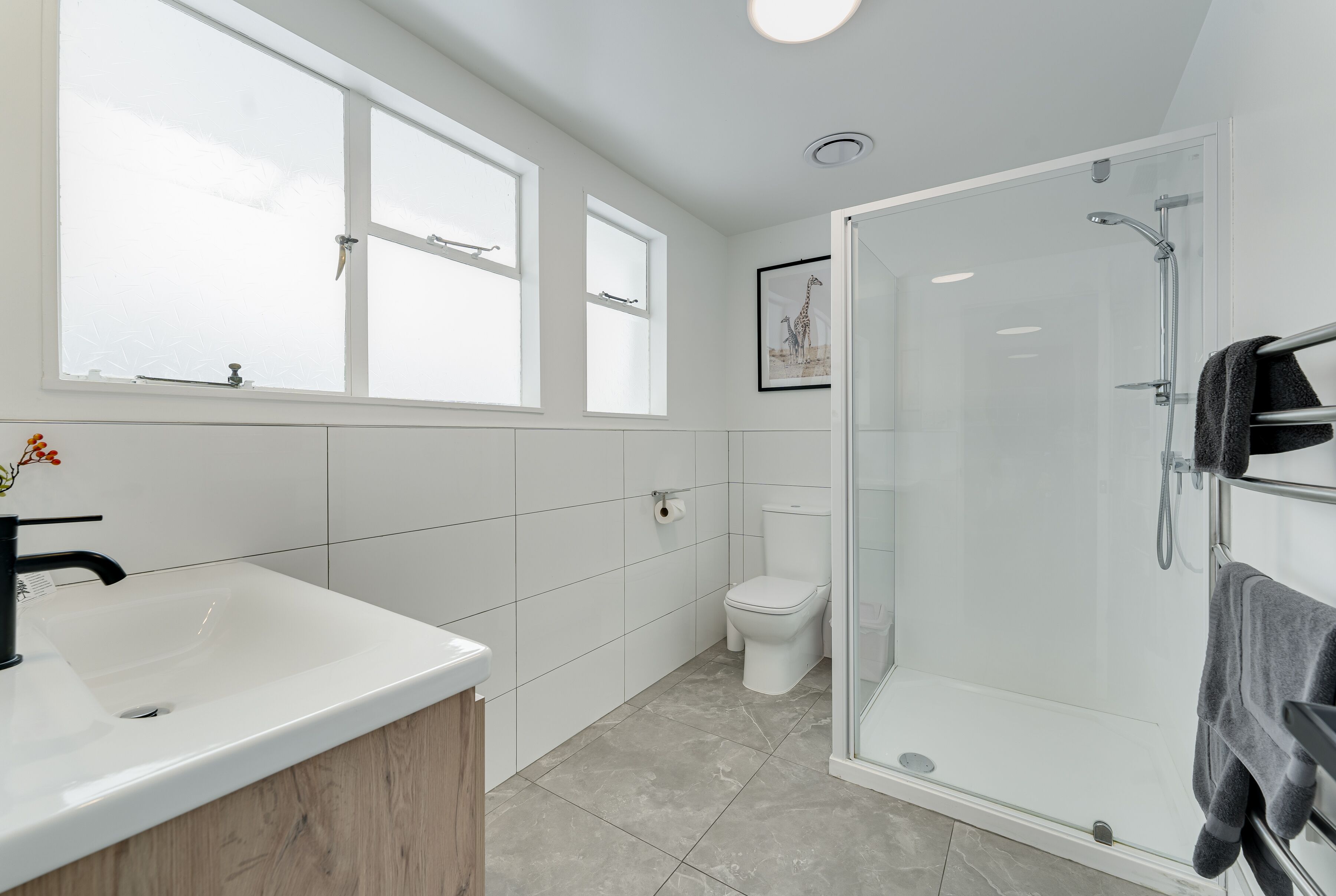 A modern bathroom with a large white sink, a glass-enclosed shower, and a toilet.