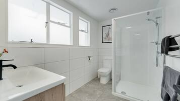 Un baño moderno con un lavamanos grande de color blanco, una ducha con mampara de vidrio y un inodoro.