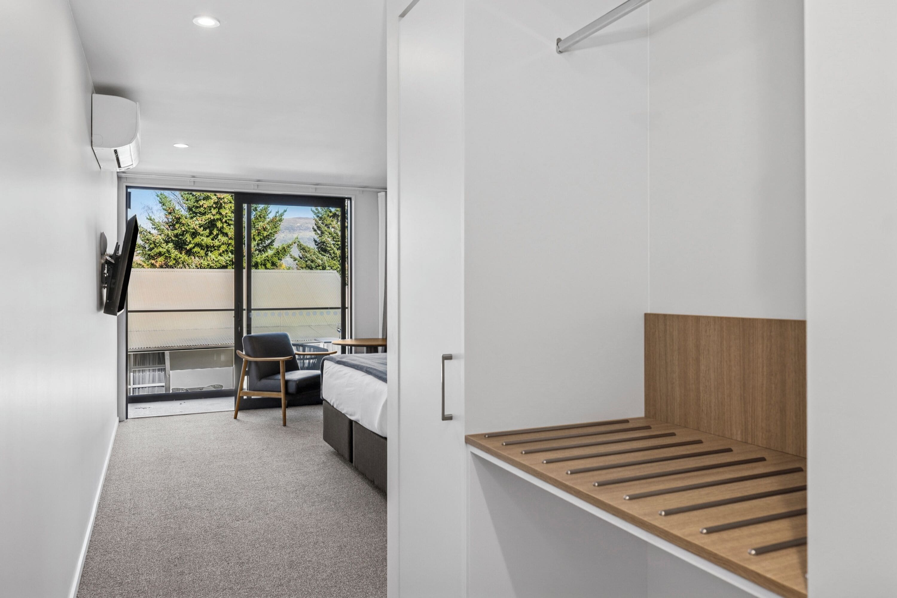 A modern bedroom with a bed, a chair, a TV, and a balcony with a view.