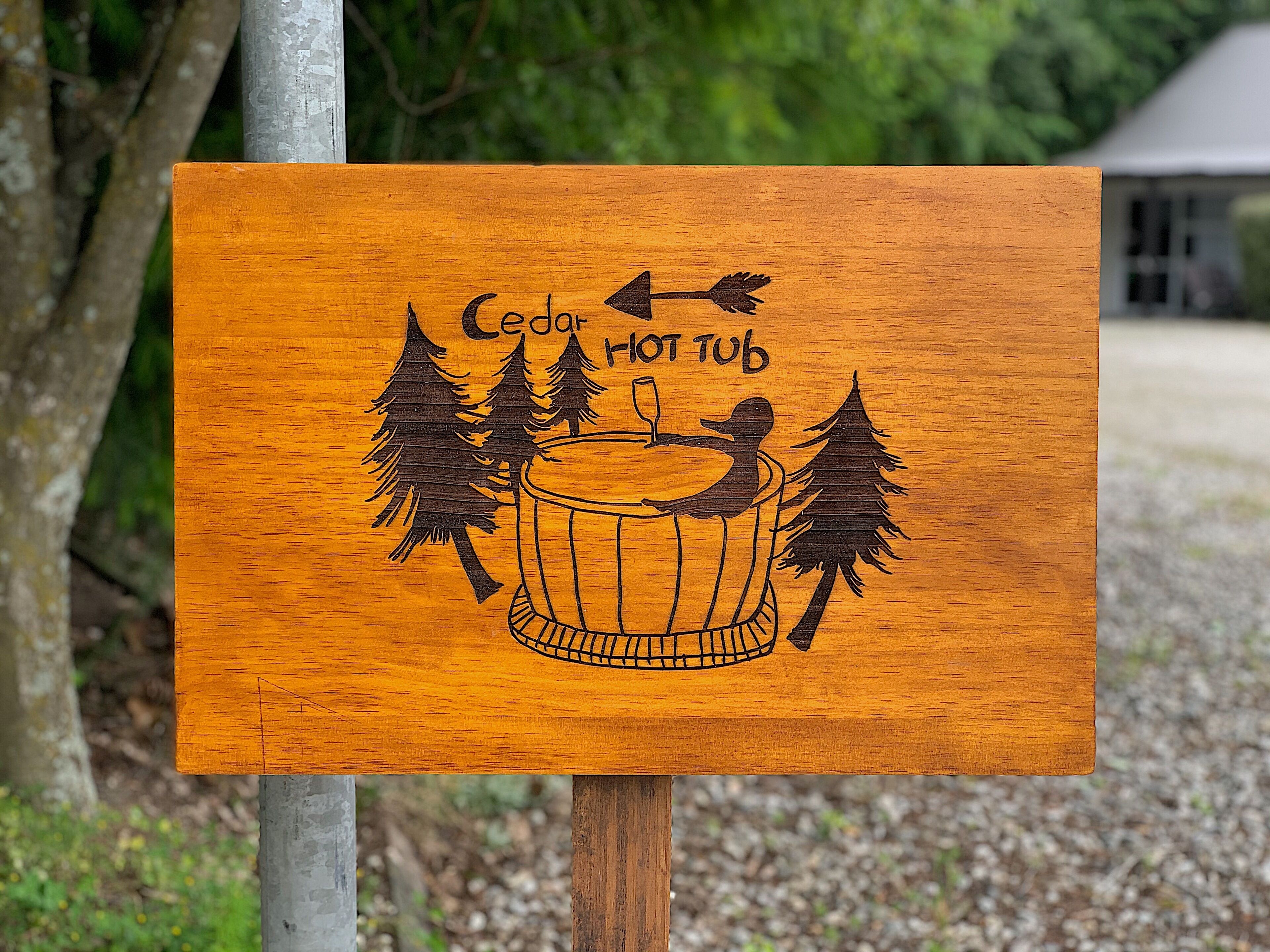 Een houten bord met een afbeelding van een hottub en de tekst 'Cedar Hot Tub'.