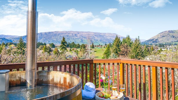 Un jacuzzi en una terraza de madera con una vista panorámica de las montañas al fondo.