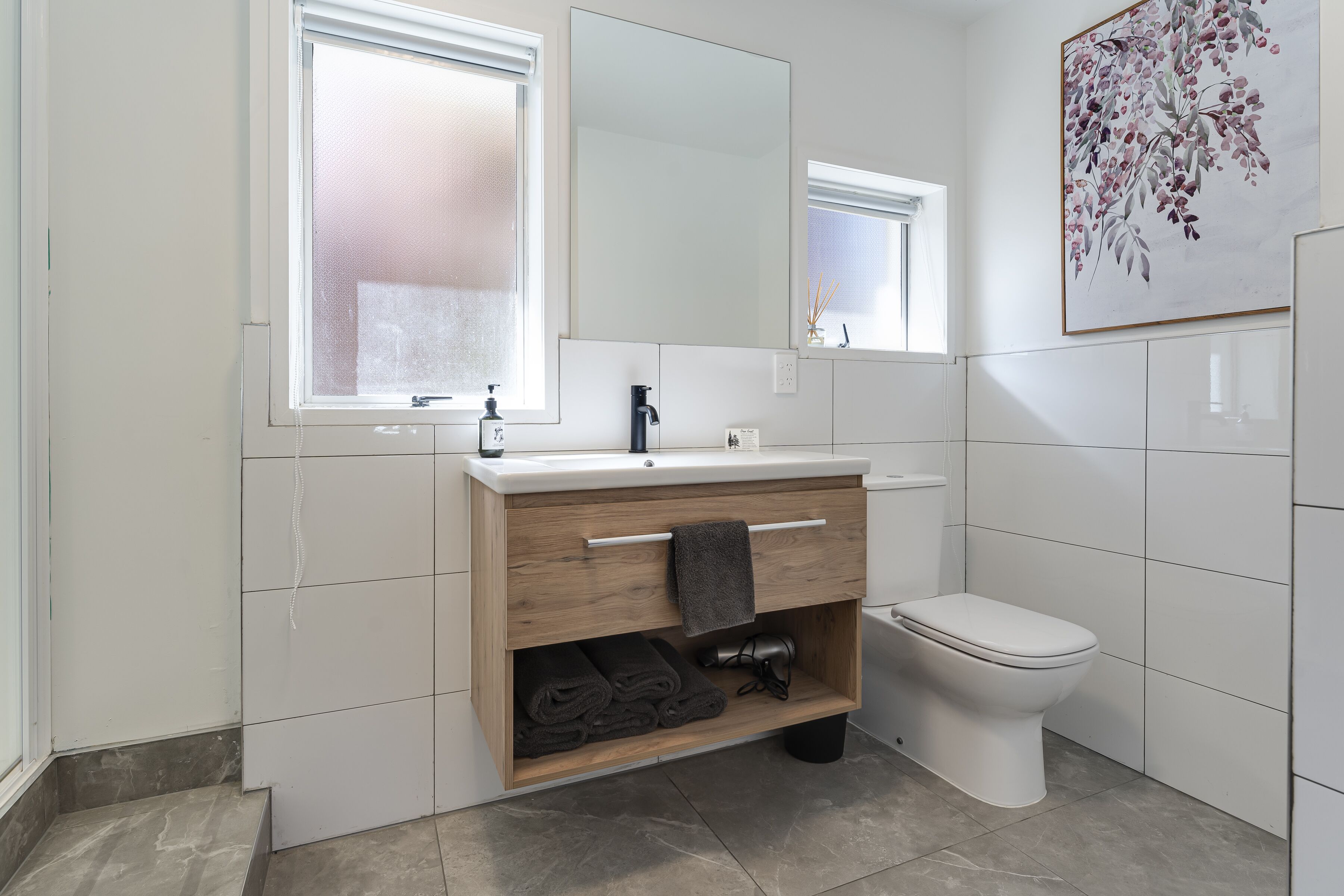 A modern bathroom with a wooden vanity, a toilet, and a large mirror.