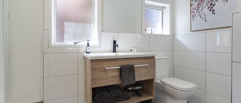 A modern bathroom with a wooden vanity, a toilet, and a large mirror.