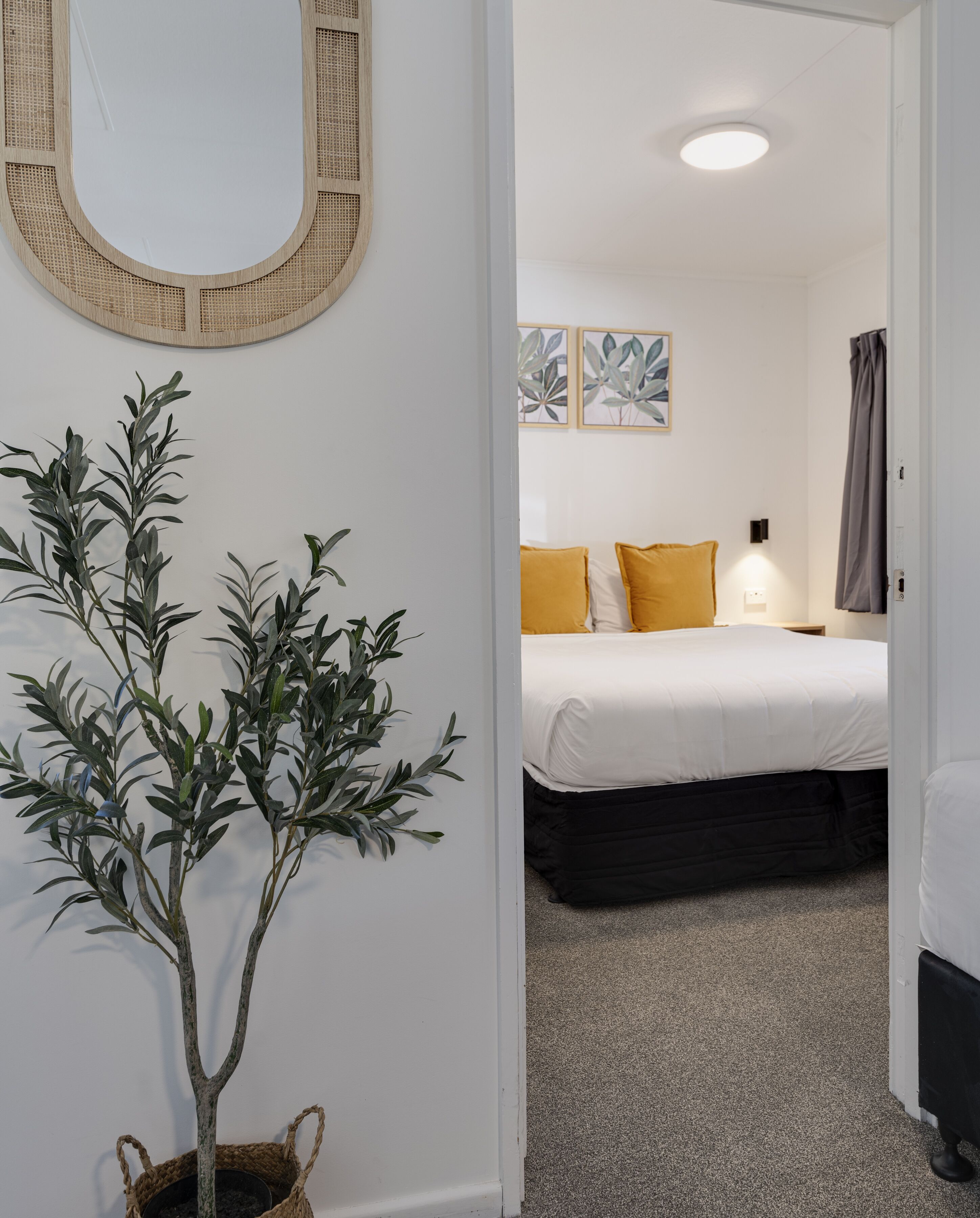 A hotel room with a bed, a bedside table, a lamp, and a potted plant.