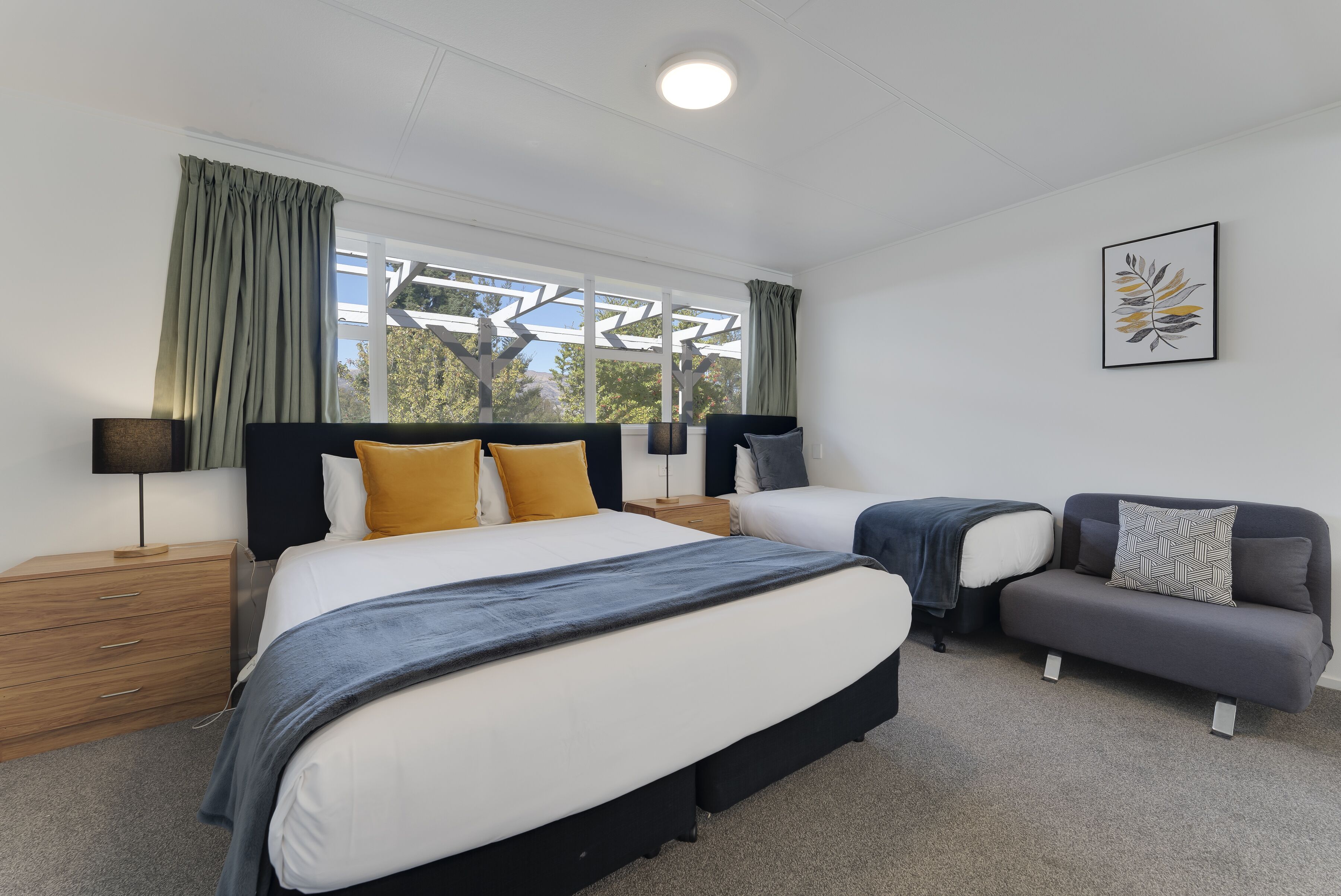 A modern bedroom with two beds, a sofa, and a large window with curtains.
