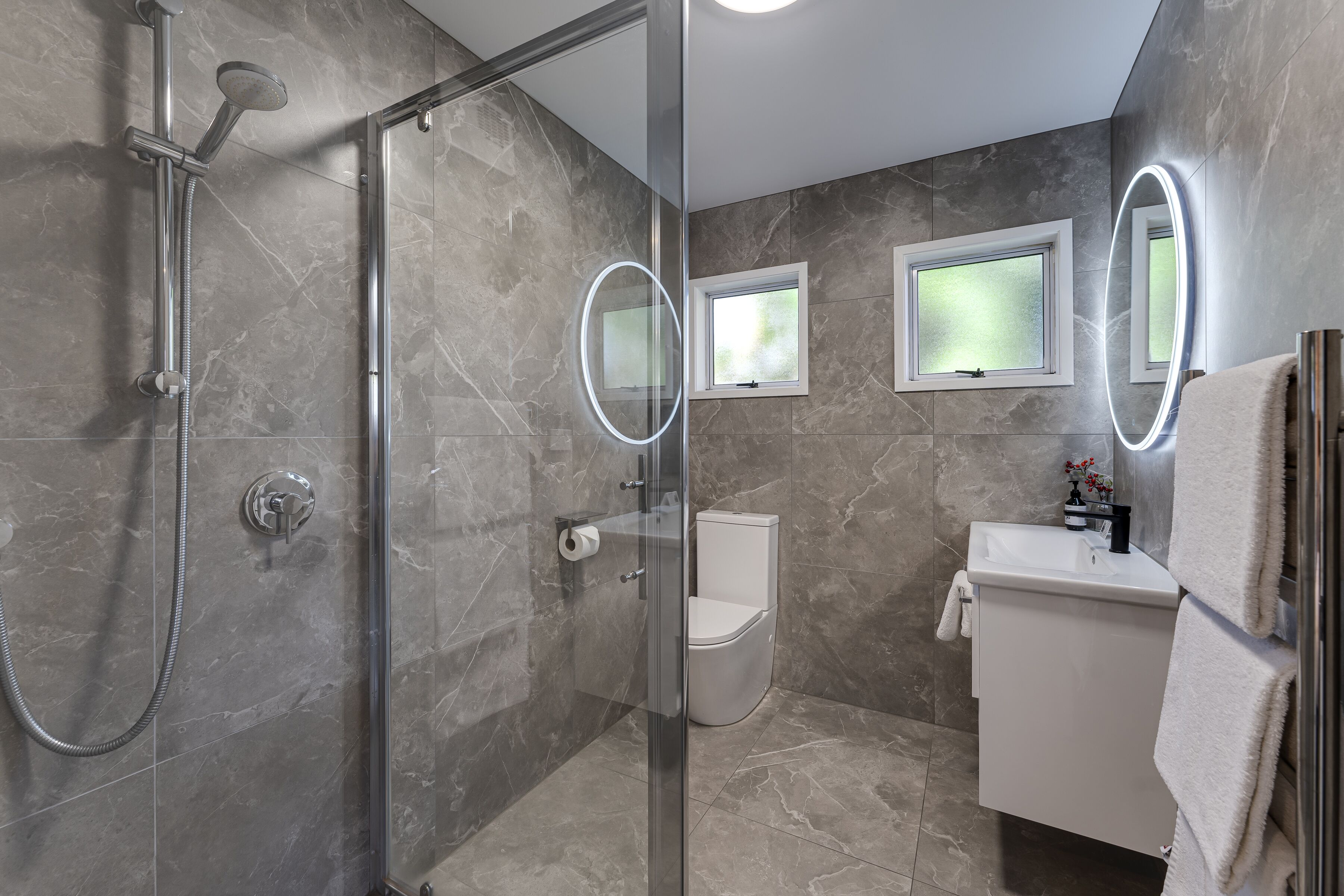 A modern bathroom with a glass-enclosed shower, a toilet, and a sink with a mirror.