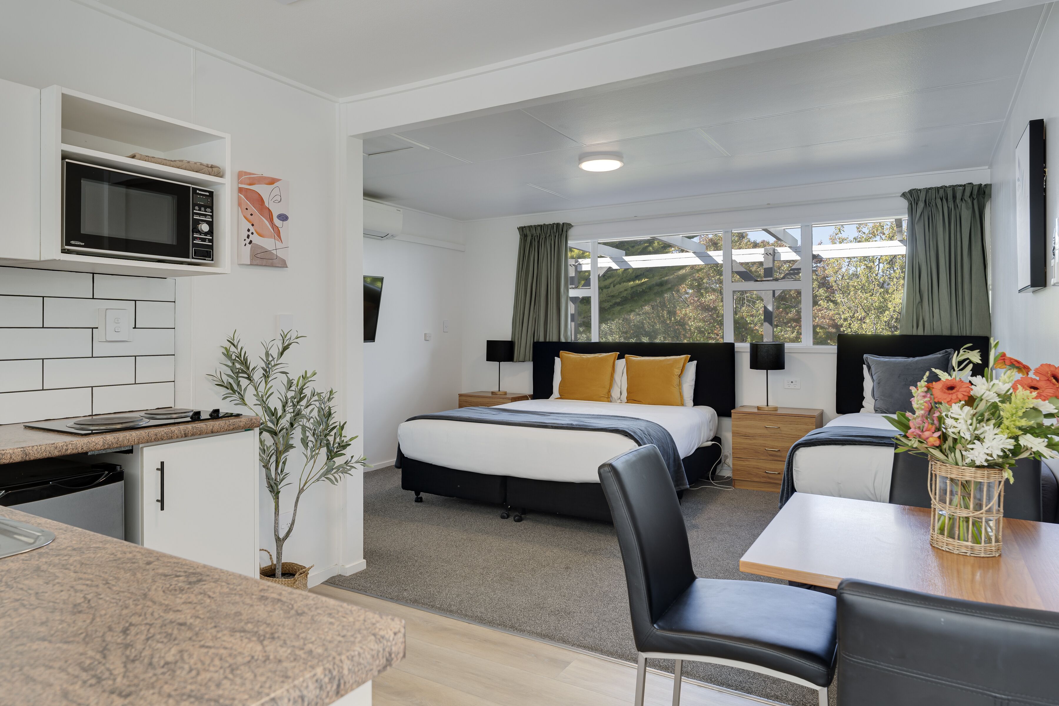 Habitación de hotel moderna con kitchenette, una cama con dos almohadas, una mesa de comedor y vistas al exterior.