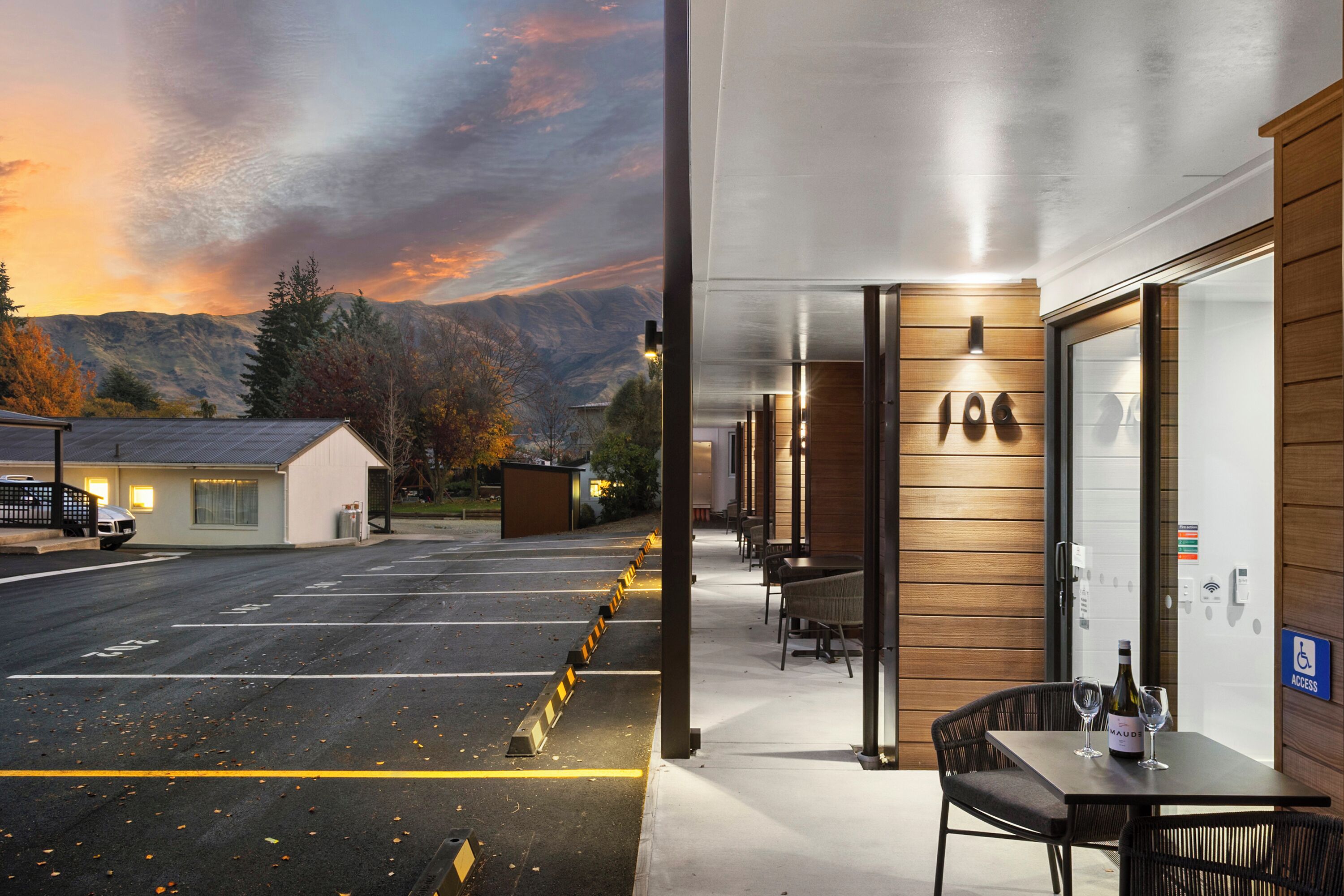 A hotel with a covered outdoor seating area, a view of mountains, and a parking lot.