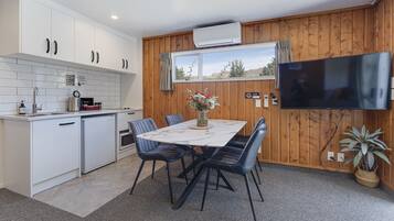 Una cocina moderna con armarios blancos, horno integrado y una zona de comedor con mesa de mármol y sillas azules.