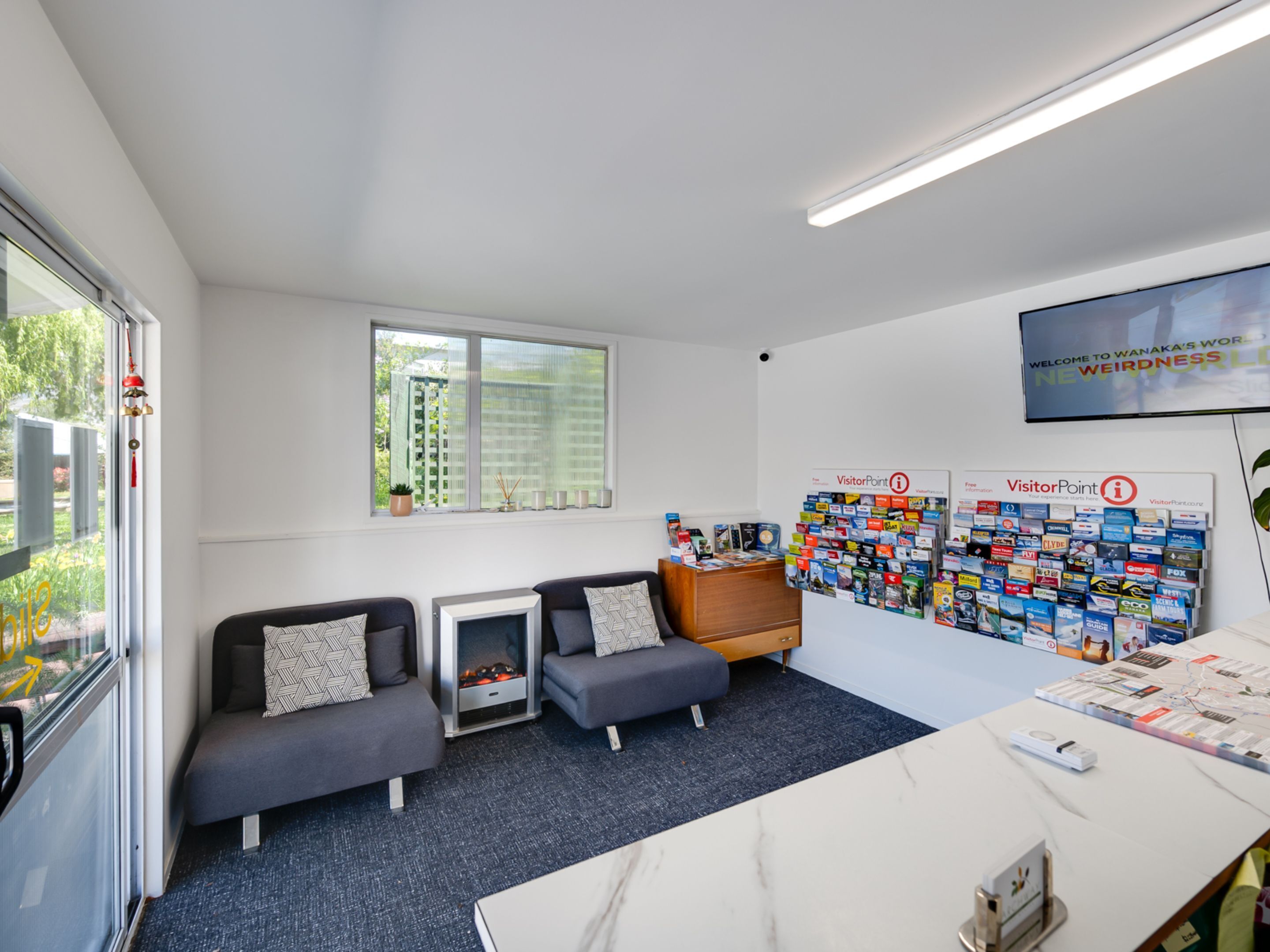 A modern office space with a reception desk, a seating area with two sofas, a fireplace, and a wall display of brochures.