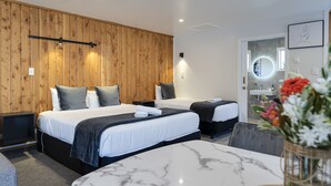 Habitación de hotel con dos camas, una mesita de mármol, un panel de pared de madera, un lavamanos pequeño y un espejo.