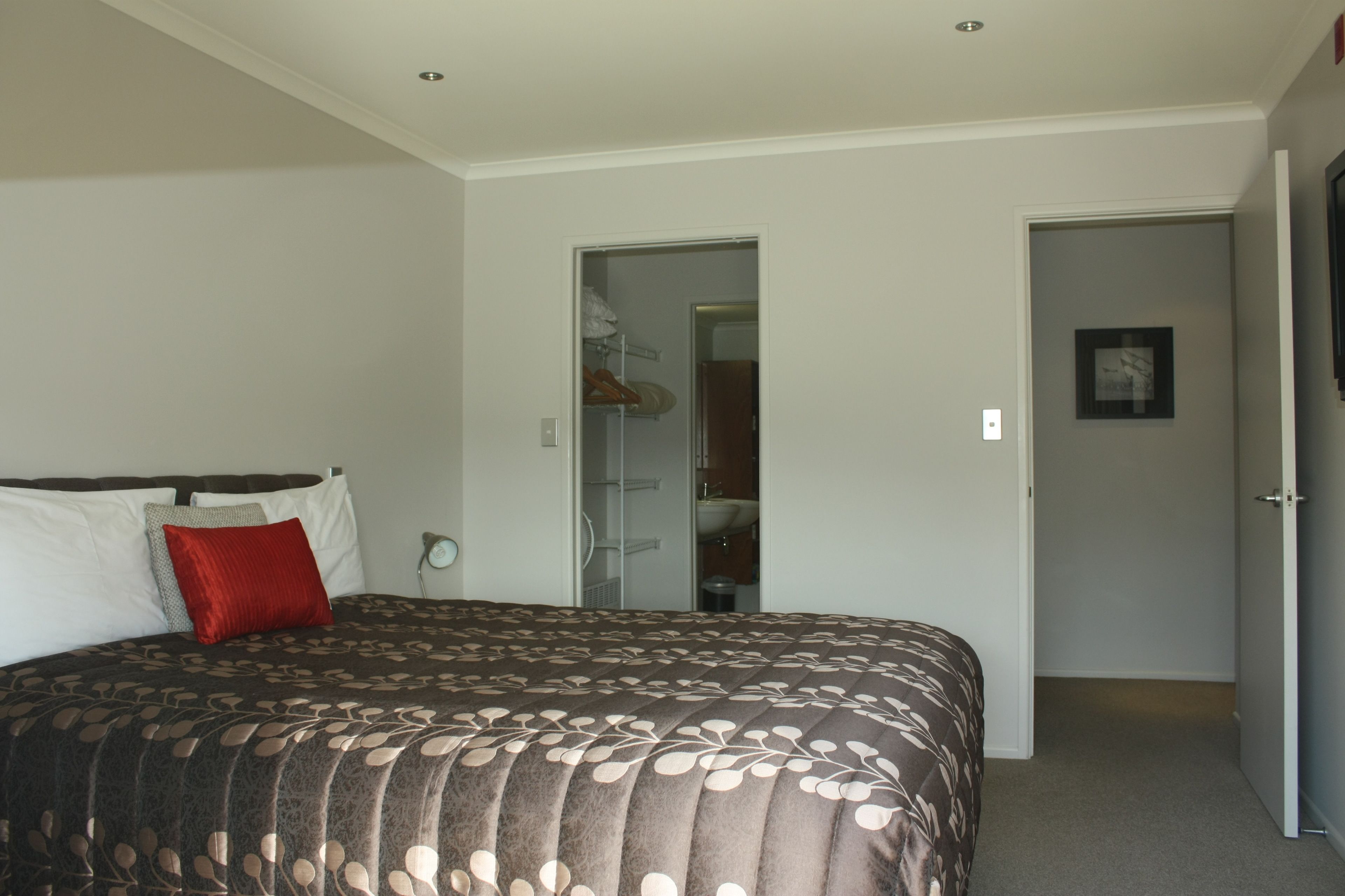 A bedroom with a large bed, a closet with hanging clothes, and a bathroom visible through an open door.