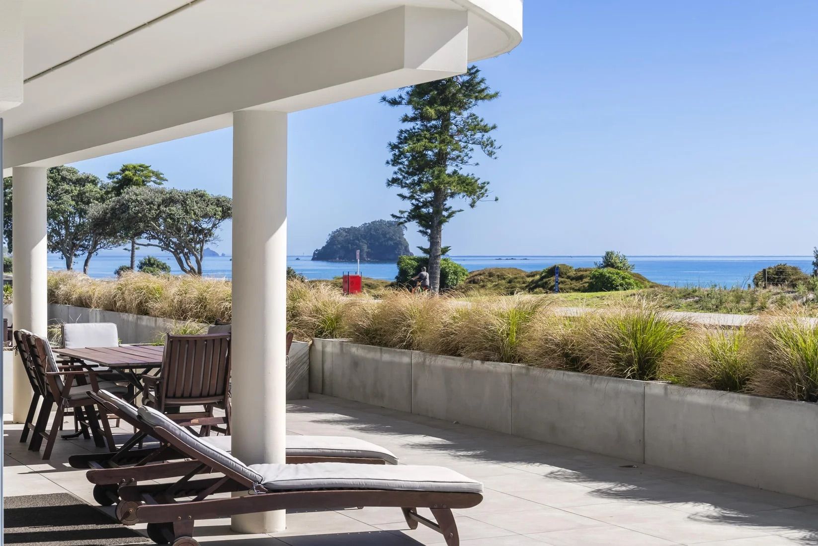 A covered outdoor seating area with lounge chairs and a view of the sea.