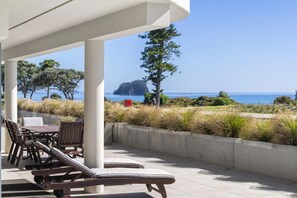 A covered outdoor seating area with lounge chairs and a view of the sea. - The Reef Beachfront Apartments (Tauranga)