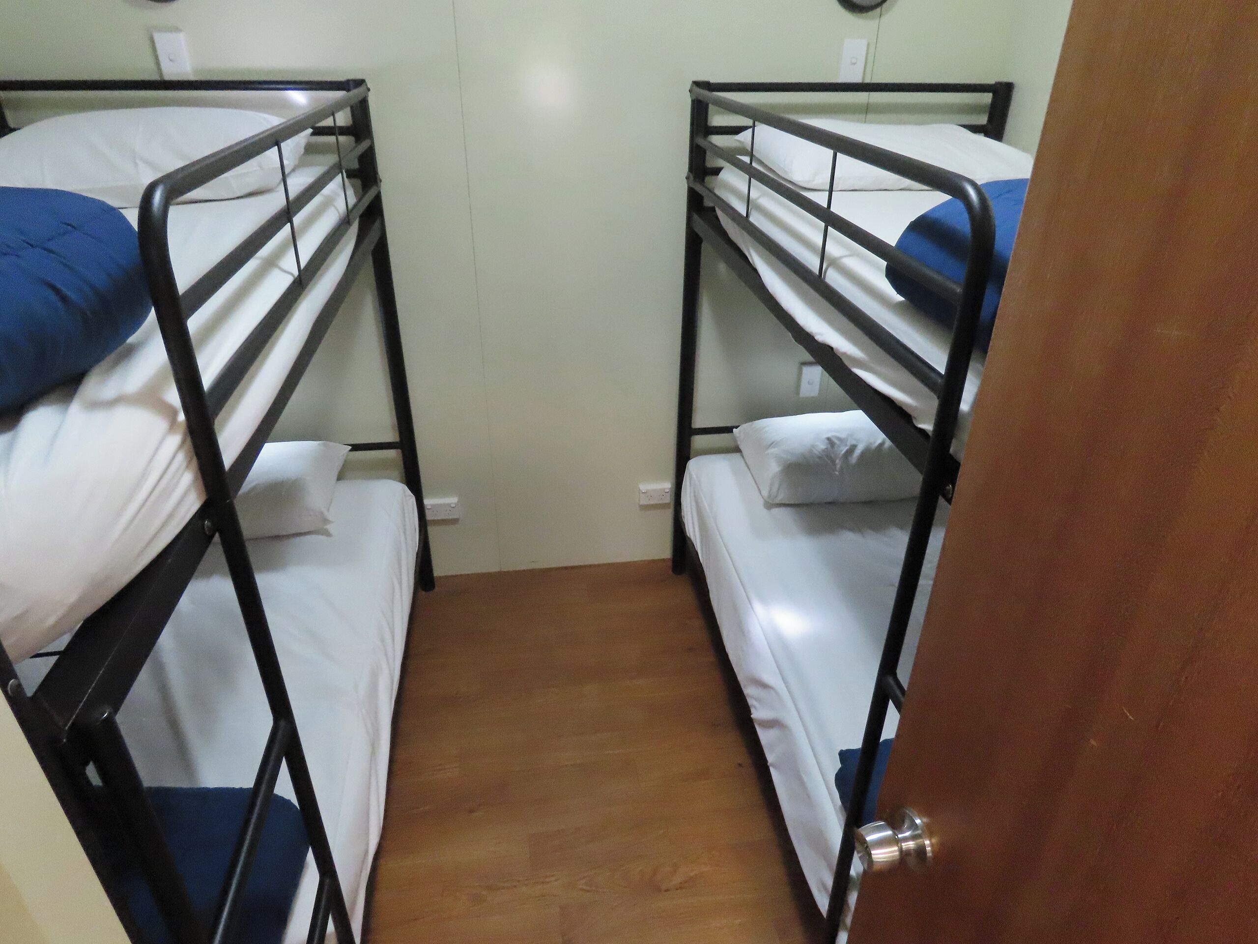 A room with two bunk beds, each with a pillow and a blanket.