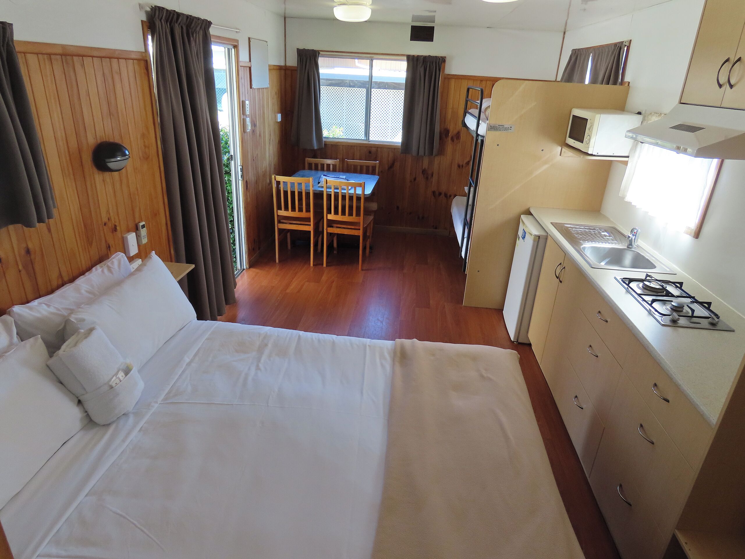 A compact room with a bed, a small kitchenette, a dining area, and a window with curtains.