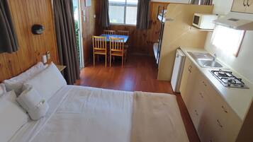 A compact room with a bed, a small kitchenette, a dining area, and a window with curtains.